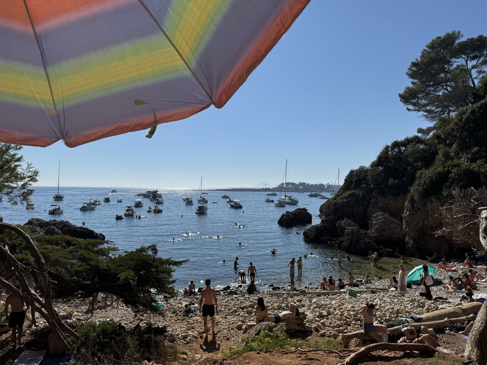 A crowded cove near Cap d'Antibes on an August afternoon, swimmers in the water and boats anchored offshore