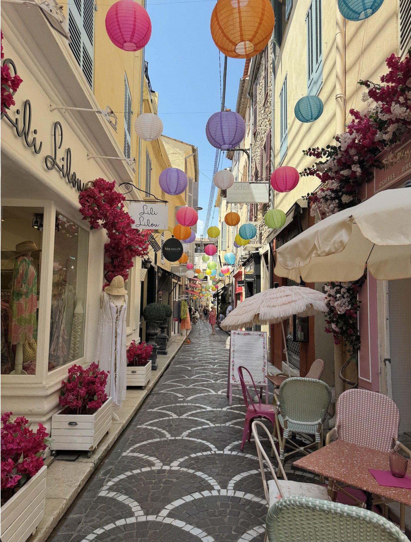 A lantern-strung pedestrian street in Antibes' old town, boutiques open and shoppers strolling