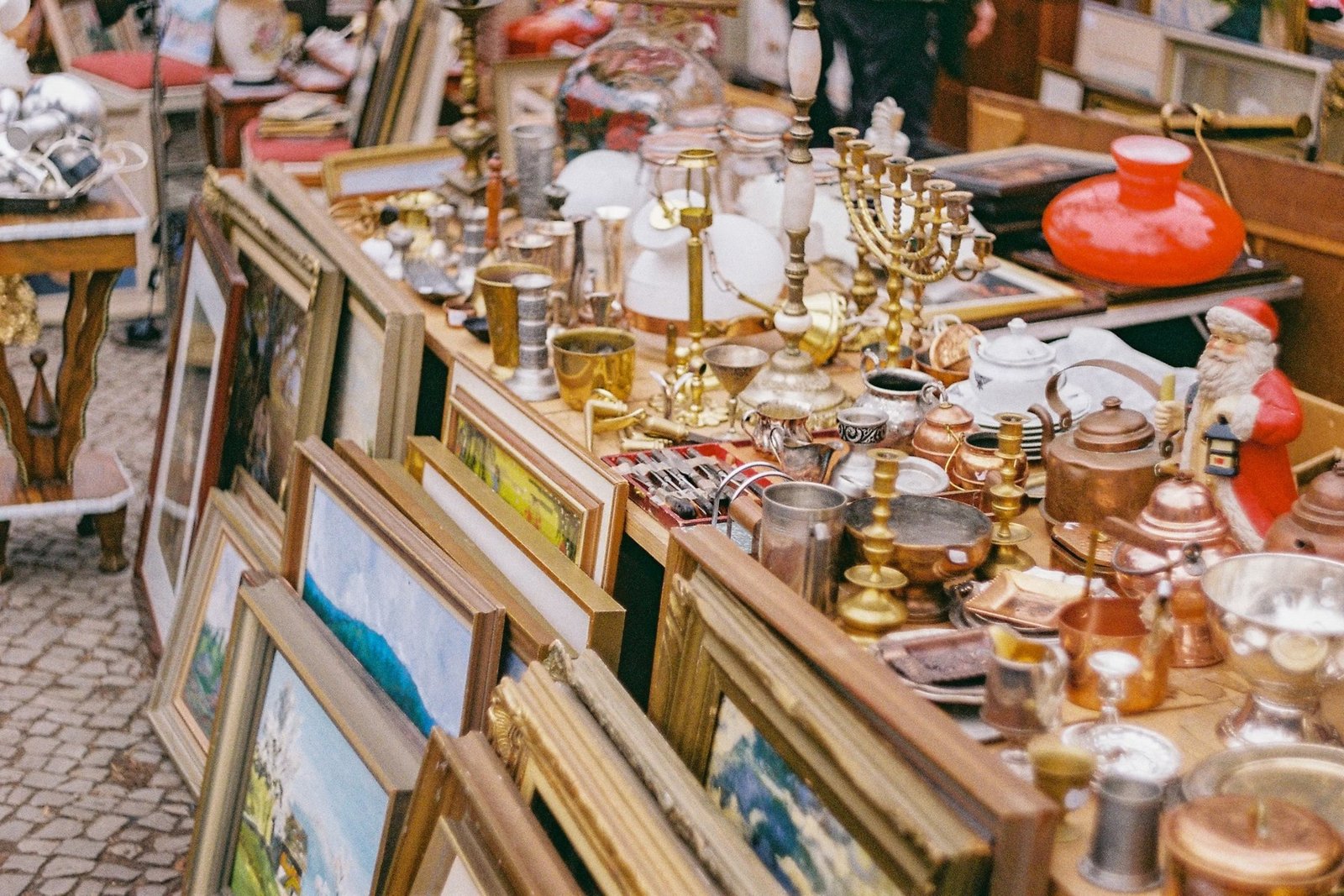 A brocante stall crowded with copperware, candelabra and framed paintings