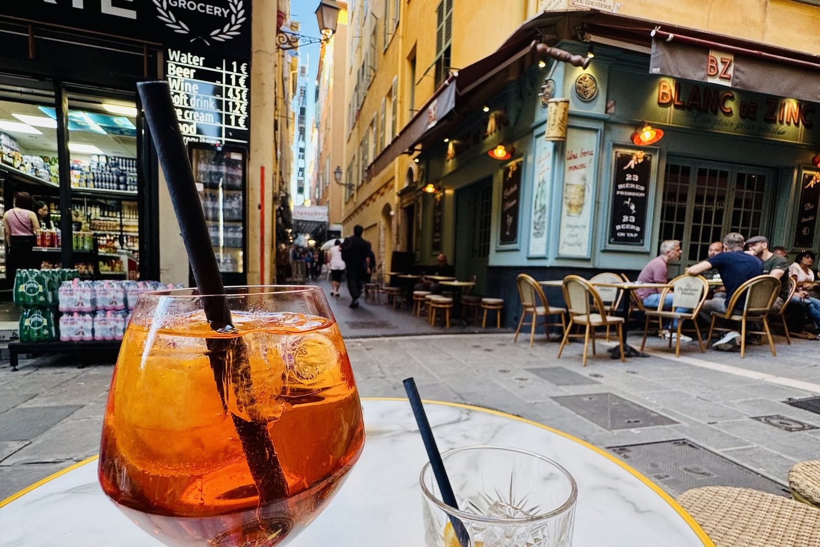 An Aperol spritz and an old fashioned on a café table in a Vieux Nice alley at dusk